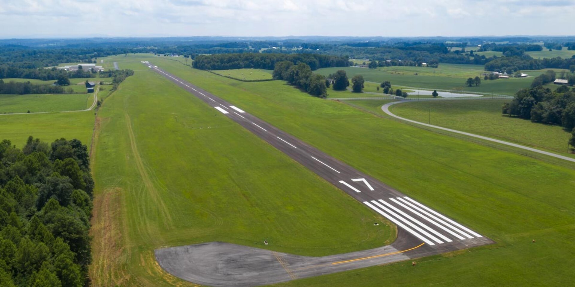 Aerial view at dusk of Russell County Airport's runway among green Kentucky hills, with the blue fingers of Lake Cumberland on the horizon