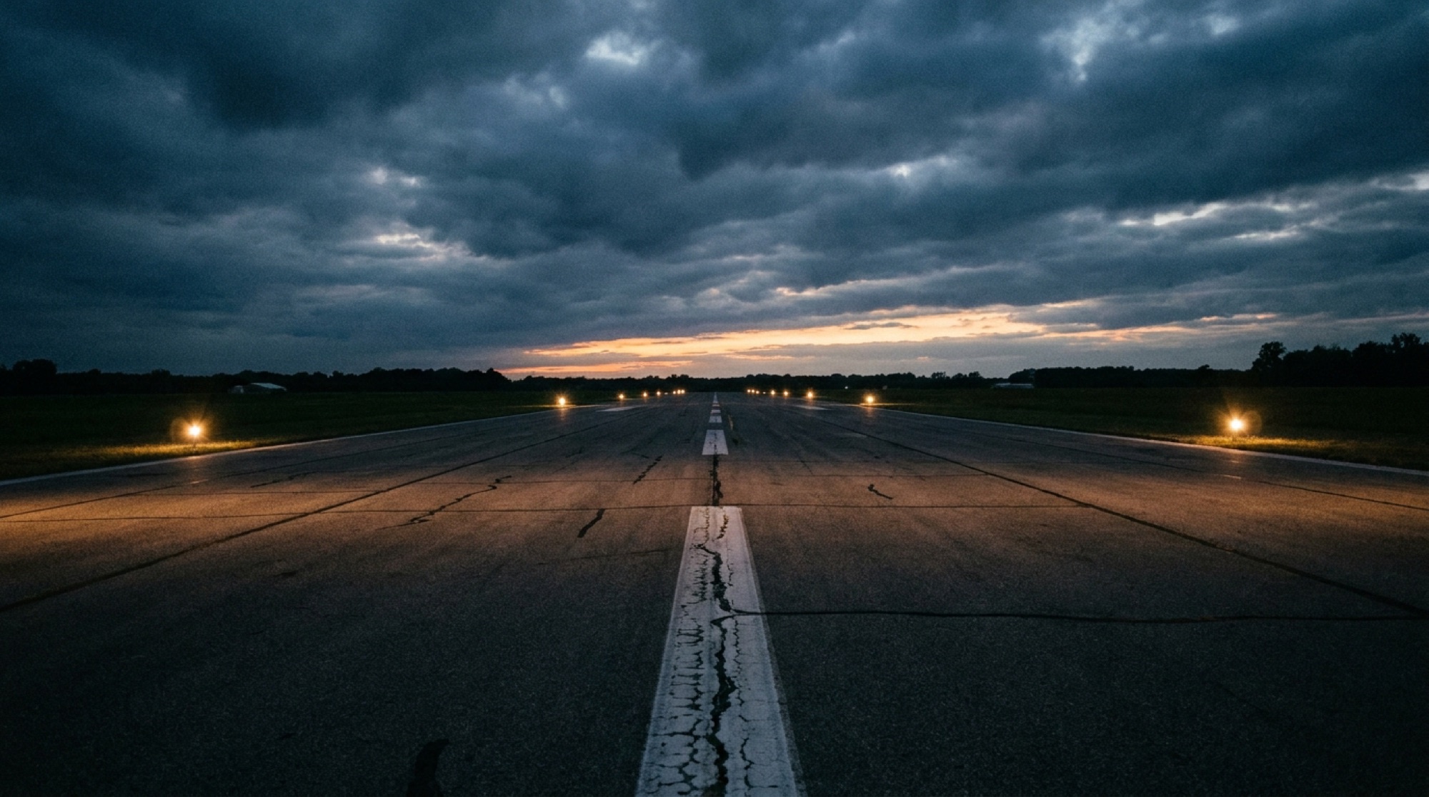 A rural airport runway at blue-hour dusk with glowing edge lights receding toward the horizon