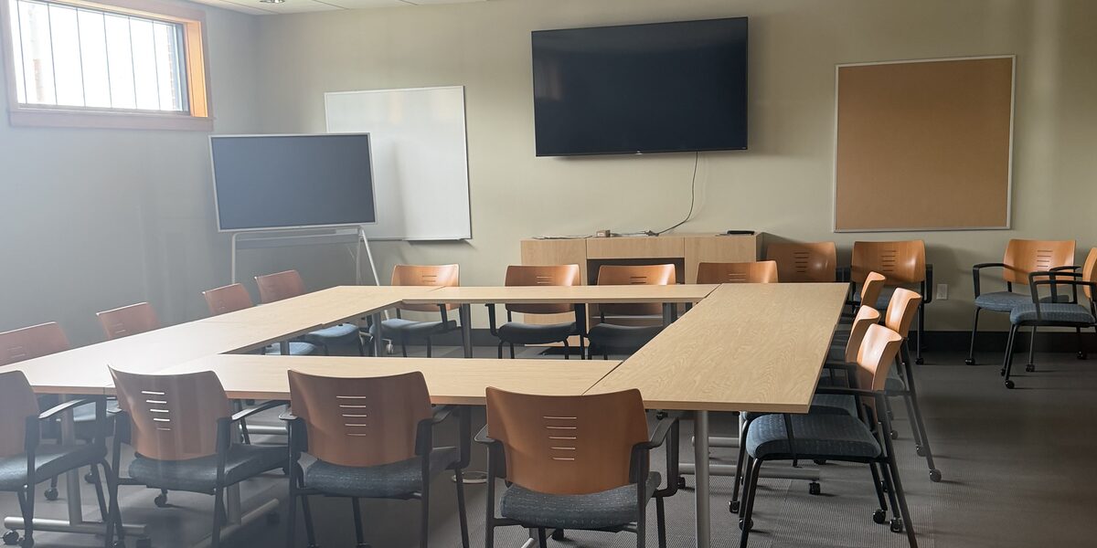The airport's conference room, with tables arranged in a hollow square, a wall-mounted display, a whiteboard and a corkboard